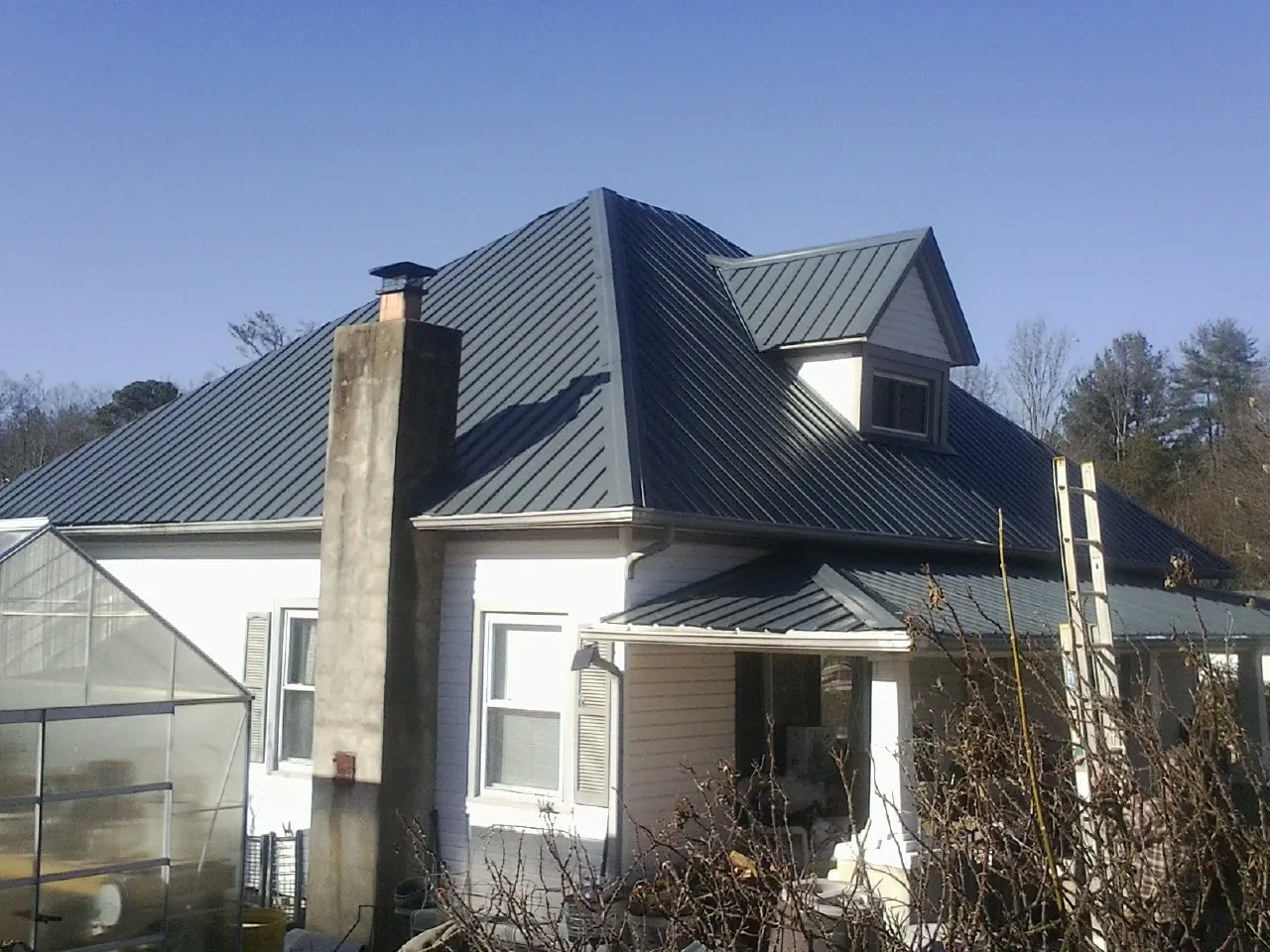 Dark blue standing seam metal roof on a white farmhouse with dormer — Slate & Tile Roof Repair by Roofing Brothers in Ware