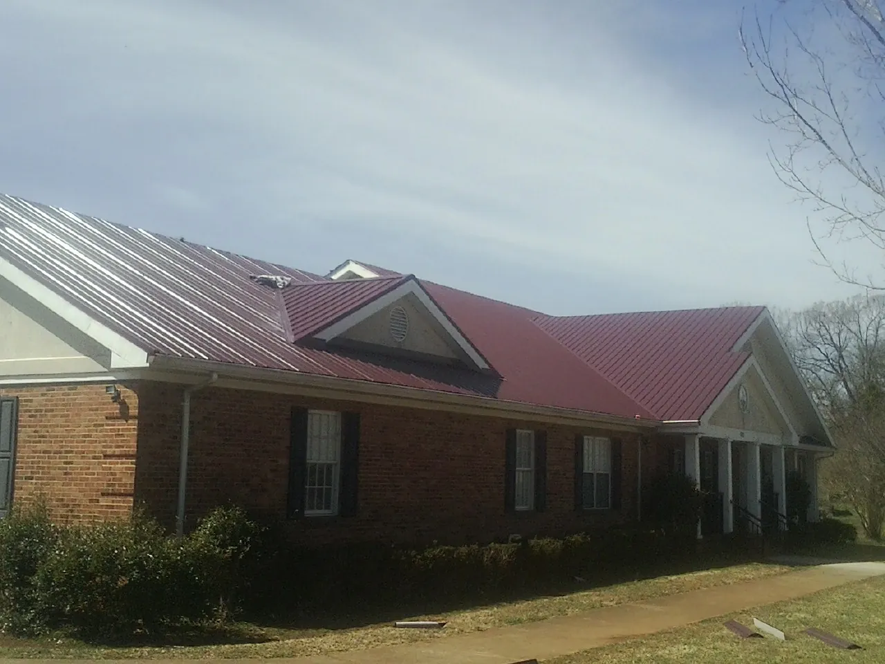 Red metal roof with gabled entries on a long brick building, from a Hail Damage Roof Repair job in Ware