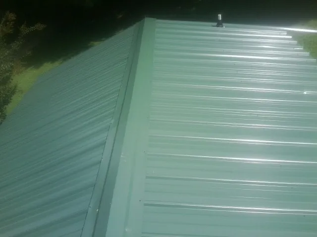 New green metal panels meeting at the ridge of a roof — Flat Roof Repair work by our crew in Ware