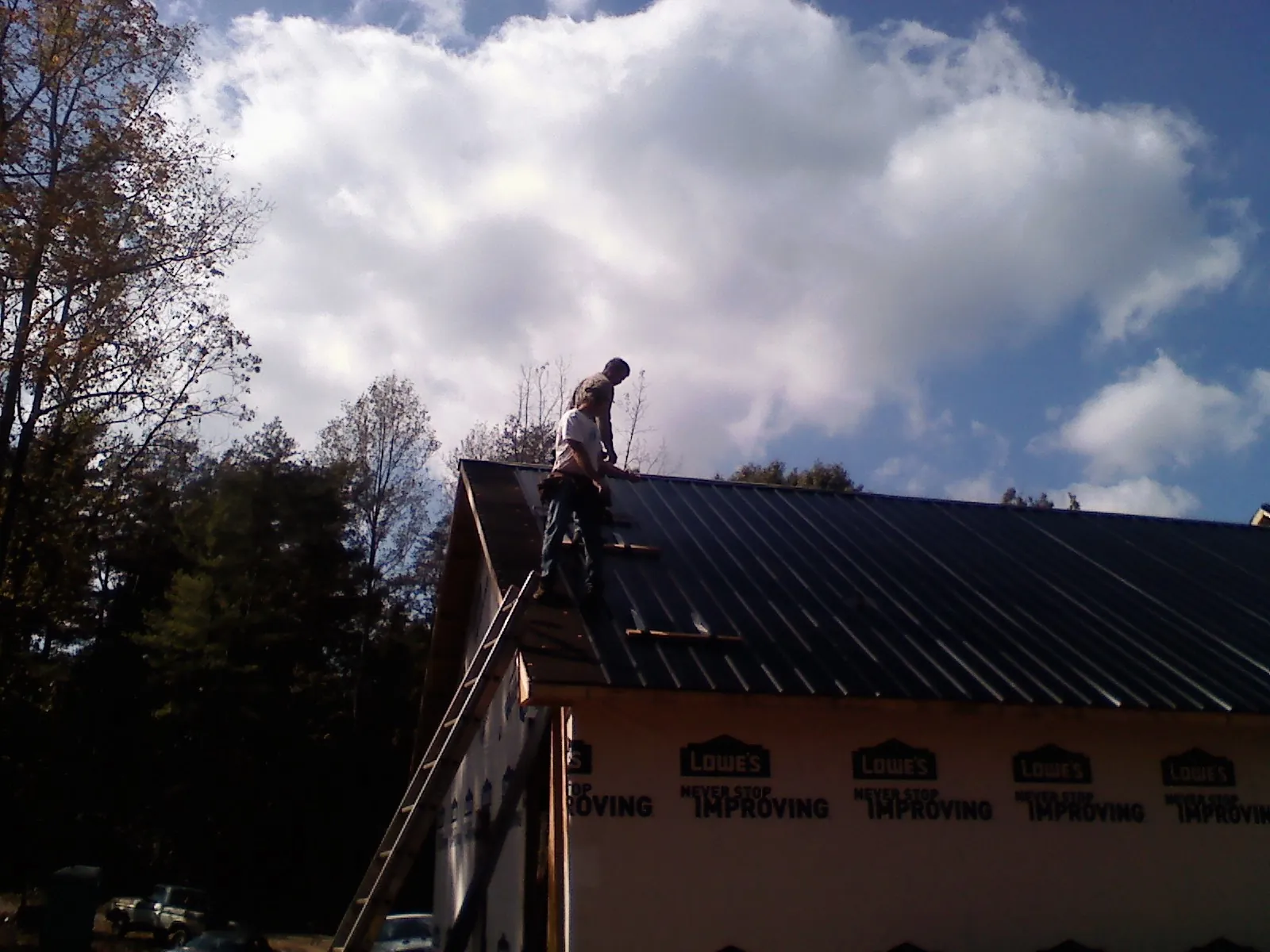 Roofer fastening dark metal panels high against a cloudy sky, from a Roof Inspection job in Ware